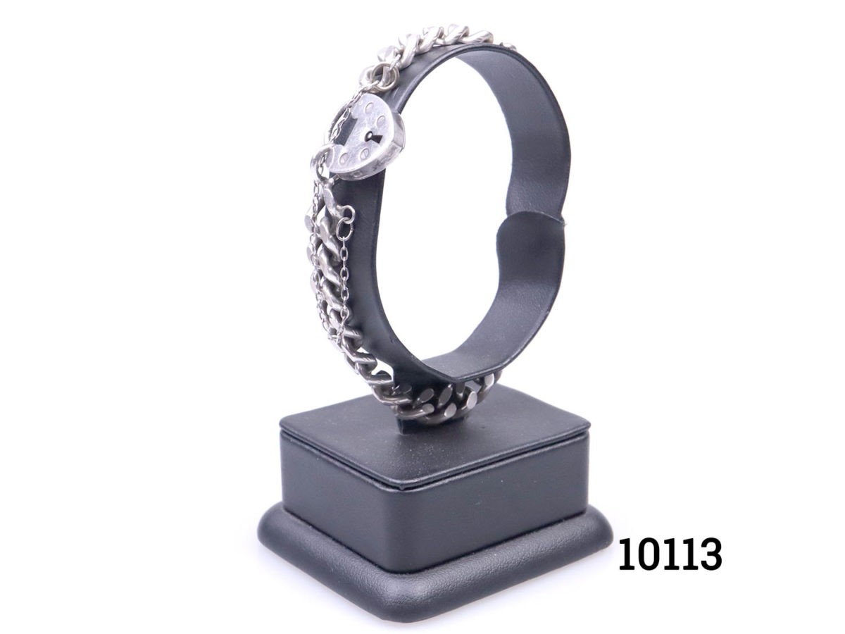 Vintage chunky sterling silver curb chain bracelet with heart shaped lock.Lion passant hallmark on one link and no hallmark on the lock. Safety chain extends opening. Lock has some signs of wear but fully functional. Photo of bracelet on display stand seen from a slight side angle