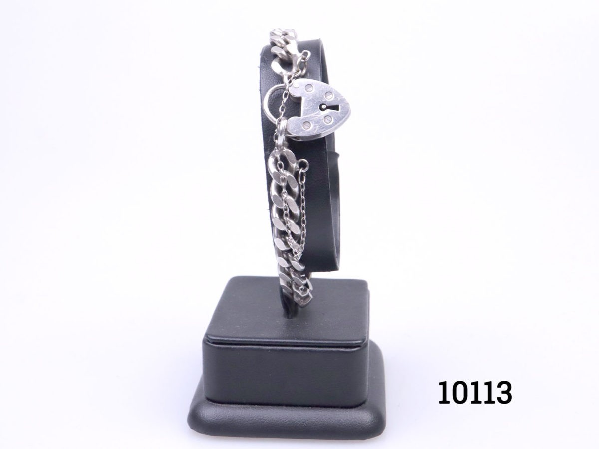 Vintage chunky sterling silver curb chain bracelet with heart shaped lock.Lion passant hallmark on one link and no hallmark on the lock. Safety chain extends opening. Lock has some signs of wear but fully functional. Main photo of bracelet displayed on a stand with the heart lock to the foreground