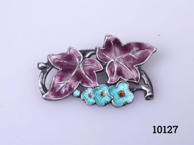 Vintage silver brooch with enamelled floral frontage. Hallmarked silver to the back. Main photo of brooch front with purple leaves at the top and light blue flowers below