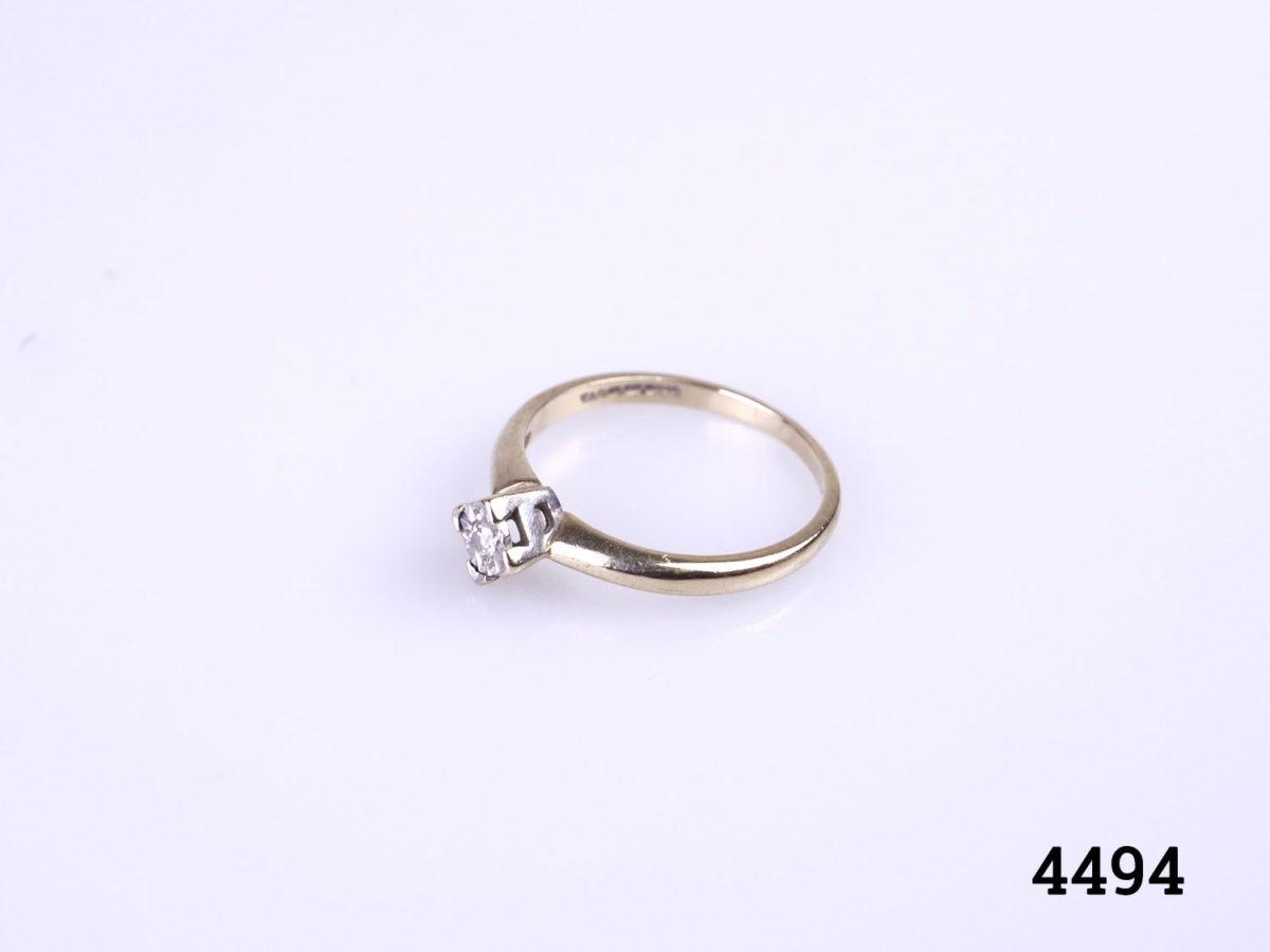 Vintage 9 karat gold ring with a small round cut diamond set on a white gold head. Ring size M / 6. Ring weight 1.8 grams. Photo of ring on a flat surface seen from a raised and slightly side angle
