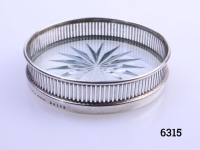 Small sterling silver edged coaster with a glass bottom. Decorated on the glass bottom with a hexadecagon design to the base (16 sided star). Hallmarked to outside rim of the silver side for sterling silver. Assayed in Birmingham. Measures 70mm in diameter. Main photo of coaster seen from a near eye level angle