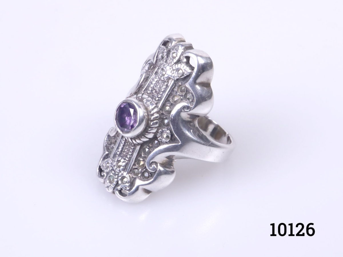 Vintage sterling silver ring set with a small amethyst coloured crystal stone to the centre. Hallmarked 925 on the back of ring front. Ring front measures 30mm by 15mm. Size P / 7.5 Photo of ring on a flat surface and seen with the ring front facing left