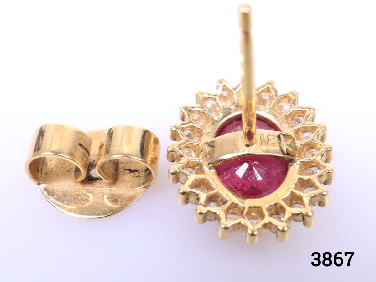 Modern 18 karat yellow gold stud earrings set with oval cut ruby framed in diamonds. Stamped 18k for 18 karat gold. Earrings weigh 5.6 grams and front measures 15mm by 12mm. Box included. Photo of back of one earring showing the 18 karat hallmark