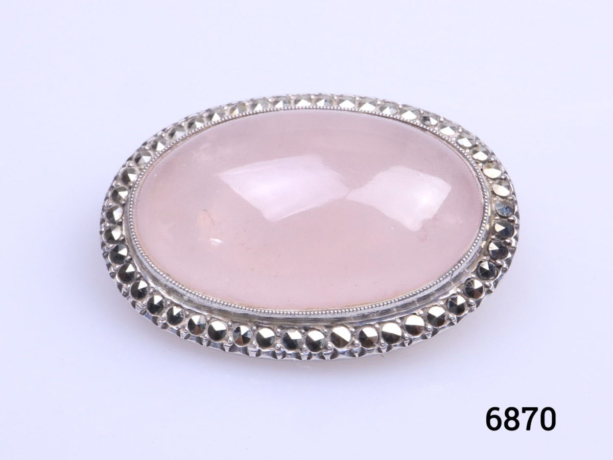 Sterling silver oval brooch set with rose quartz cabochon to the centre in a marcasite frame. Trombone clasp for added security. Close up photo of the brooch front