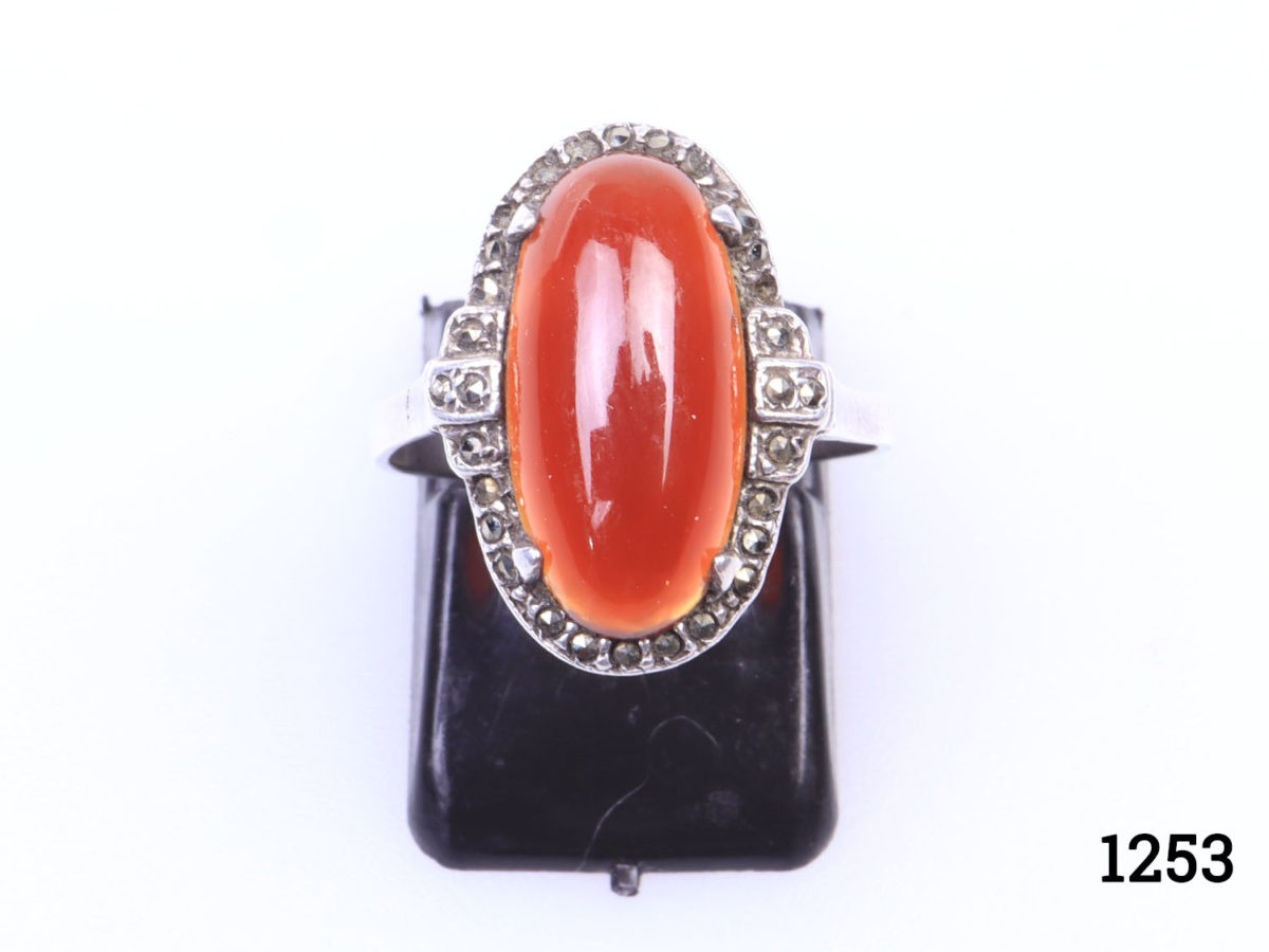 Vintage 935 silver ring set with carnelian cabochon with marcasite surround. (Some marcasite stones missing) Hallmarked 935 inside band. Ring size L.5 / 6. Ring front measures 20mm by 10mm Photo of ring seen from the front and on a display stand