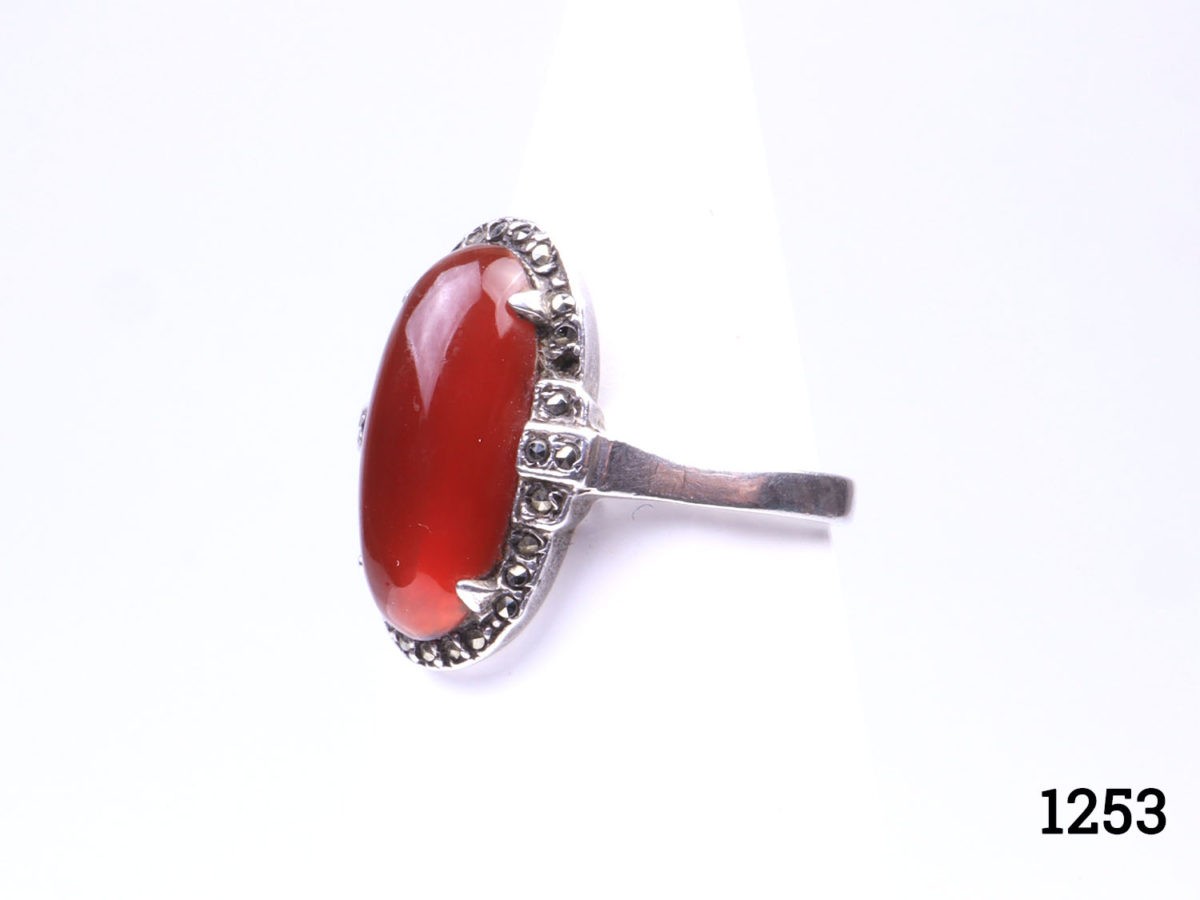 Vintage 935 silver ring set with carnelian cabochon with marcasite surround. (Some marcasite stones missing) Hallmarked 935 inside band. Ring size L.5 / 6. Ring front measures 20mm by 10mm Photo of ring seen from a slight angle with ring front to the left of picture