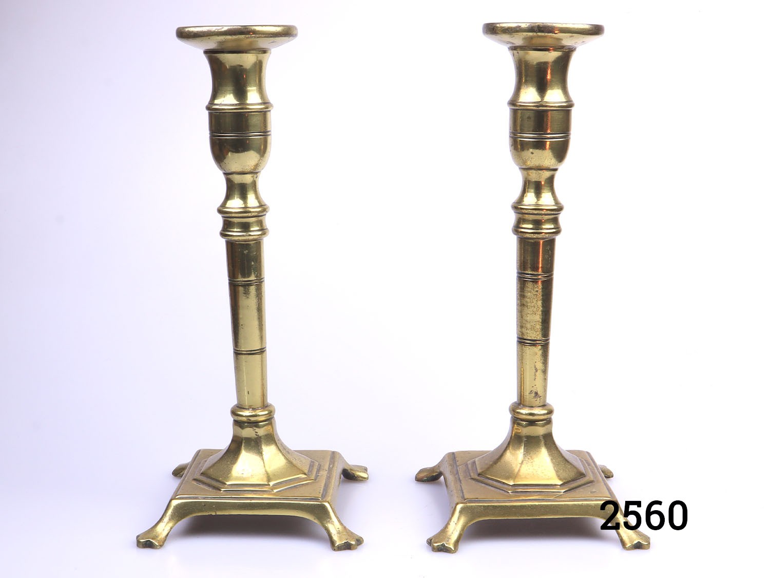 Antique pair of brass candlesticks. Each with square footed bases. c1900-c1920. Each candlestick measures 105mm square at base. Main photo of both candlesticks standing side by side
