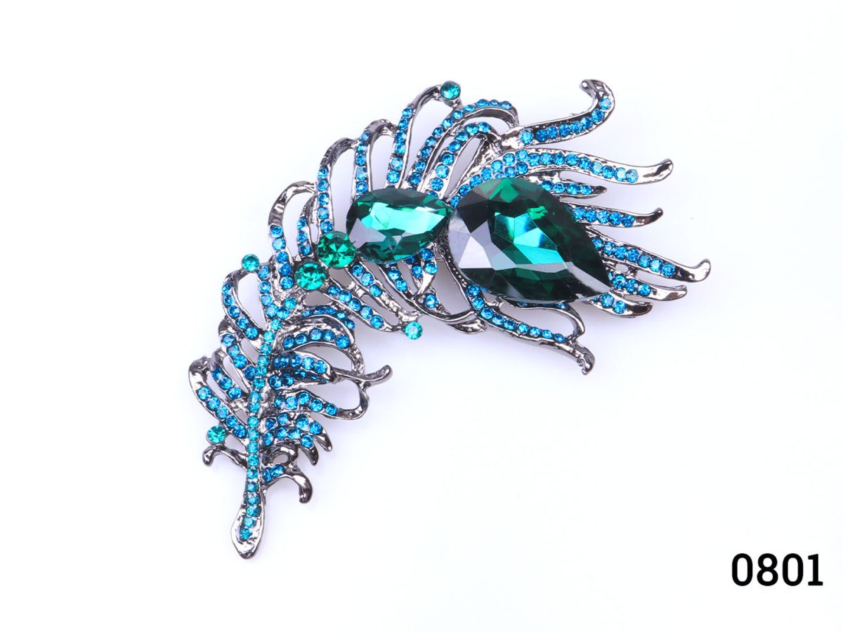 Modern large peacock feather brooch. Statement brooch in the form of a peacock feather with green glass crystals to the centre and green and turquoise smaller crystals throughout Main photo of brooch front