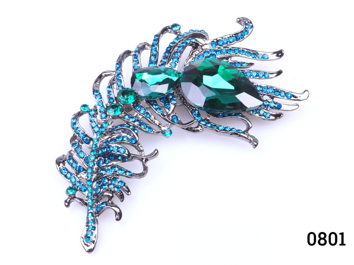 Modern large peacock feather brooch. Statement brooch in the form of a peacock feather with green glass crystals to the centre and green and turquoise smaller crystals throughout Close up photo of brooch front