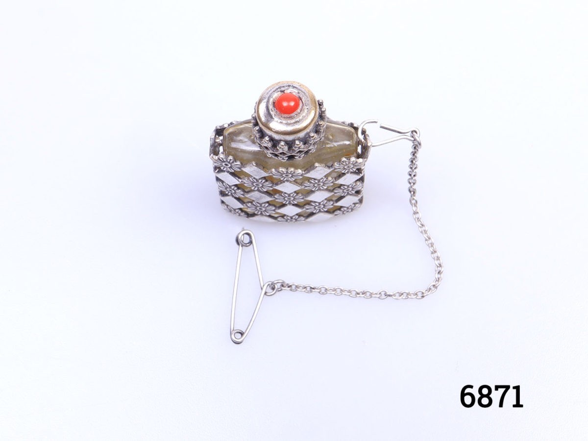 Vintage small silver perfume bottle with safety chain. Small glass perfume bottle encased in an intricate lattice work silver covering with a screw on top. Perfume applicator intact on the inner lid. Possibly a pendant previously but still could be made to be worn around the neck. No visible hallmark Photo of perfume bottle with stopper in place and seen from above showing the red stone to the top