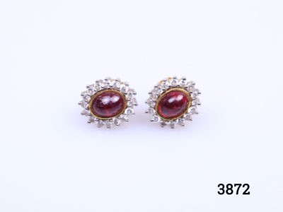 Modern 18 karat gold stud earrings each set with ruby cabochon and round cut diamonds. Front of earrings measure 11mm by 9 mm. Earrings weight 4.1 grams. Box included. Main photo of both earrings laid side by side on a flat surface