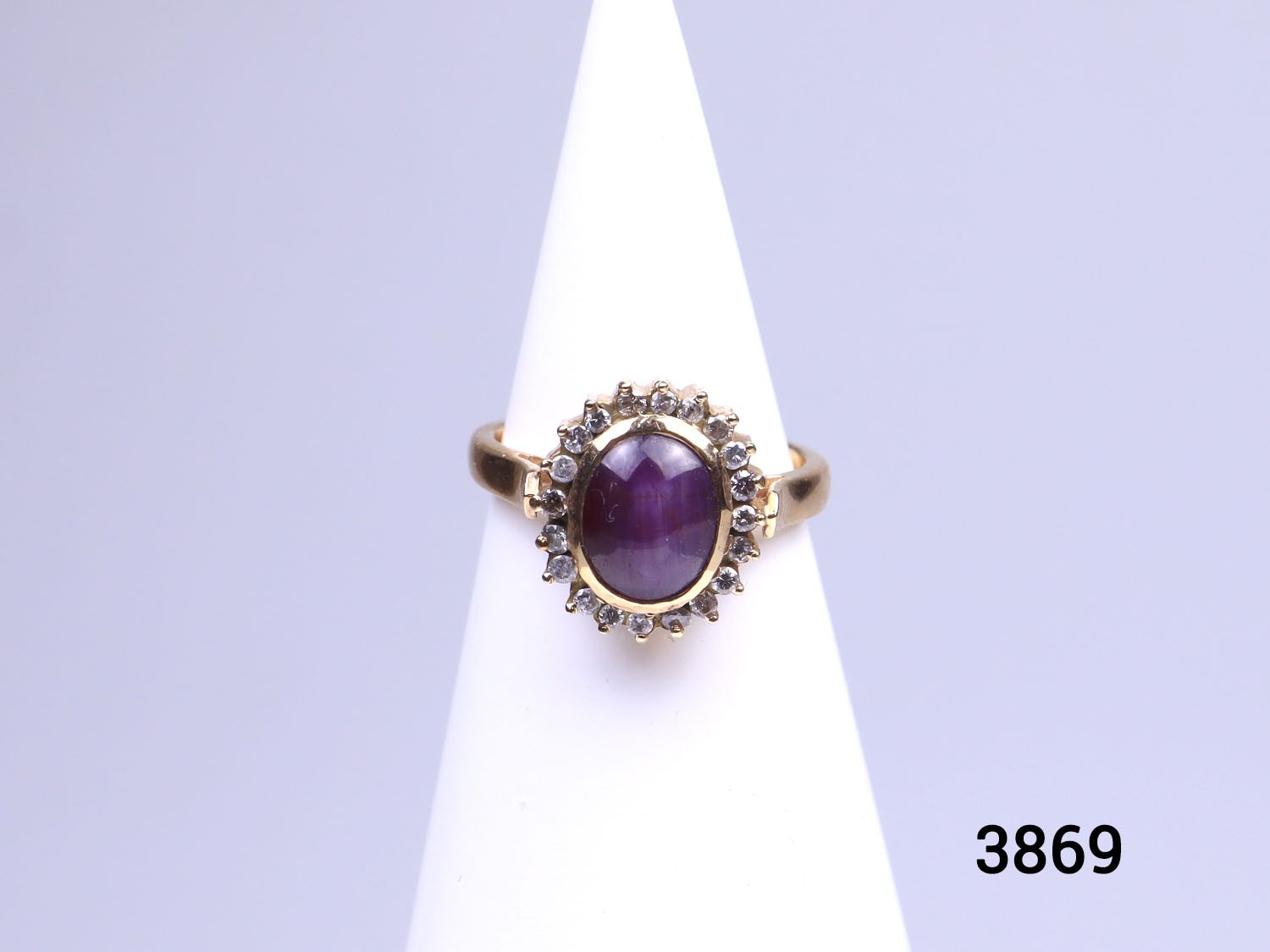 Modern 18 karat gold ring set with star ruby cabochon inside a frame of round cut diamonds. Hallmarked 18k on the inside band. Ring size N / 6.5.  Ring weight 5.9 grams.  Box included.  Main photo of ring on a white cone display stand shown straight on