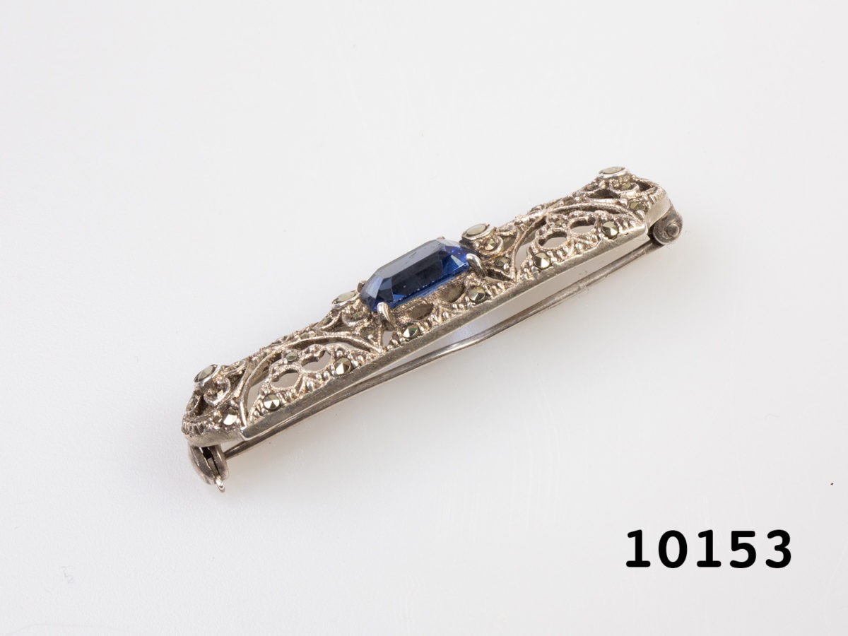 Vintage 935 silver and blue topaz brooch. Vintage brooch with a rectangle cut blue topaz to the centre of filigree and marcasite setting. Hallmarked 935 to back of brooch. Pin slightly misshapen. Photo of brooch on a flat surface and seen from side angle showing the width and misshapen pin Close up photo of the 935 hallmark to the back of brooch
