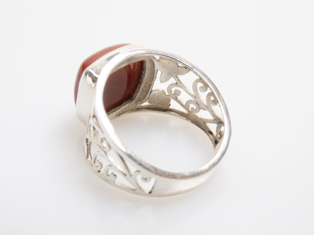 Large sterling silver and carnelian ring. Chunky looking ring with a nice sized square carnelian stone and pierced scrollwork to the shoulders. Very fine thin silver. Hallmarked 925 for sterling silver. Stone measures 12mm square.  Size V / 10.5 Photo of ring on a flat surface with the ring front facing top left corner