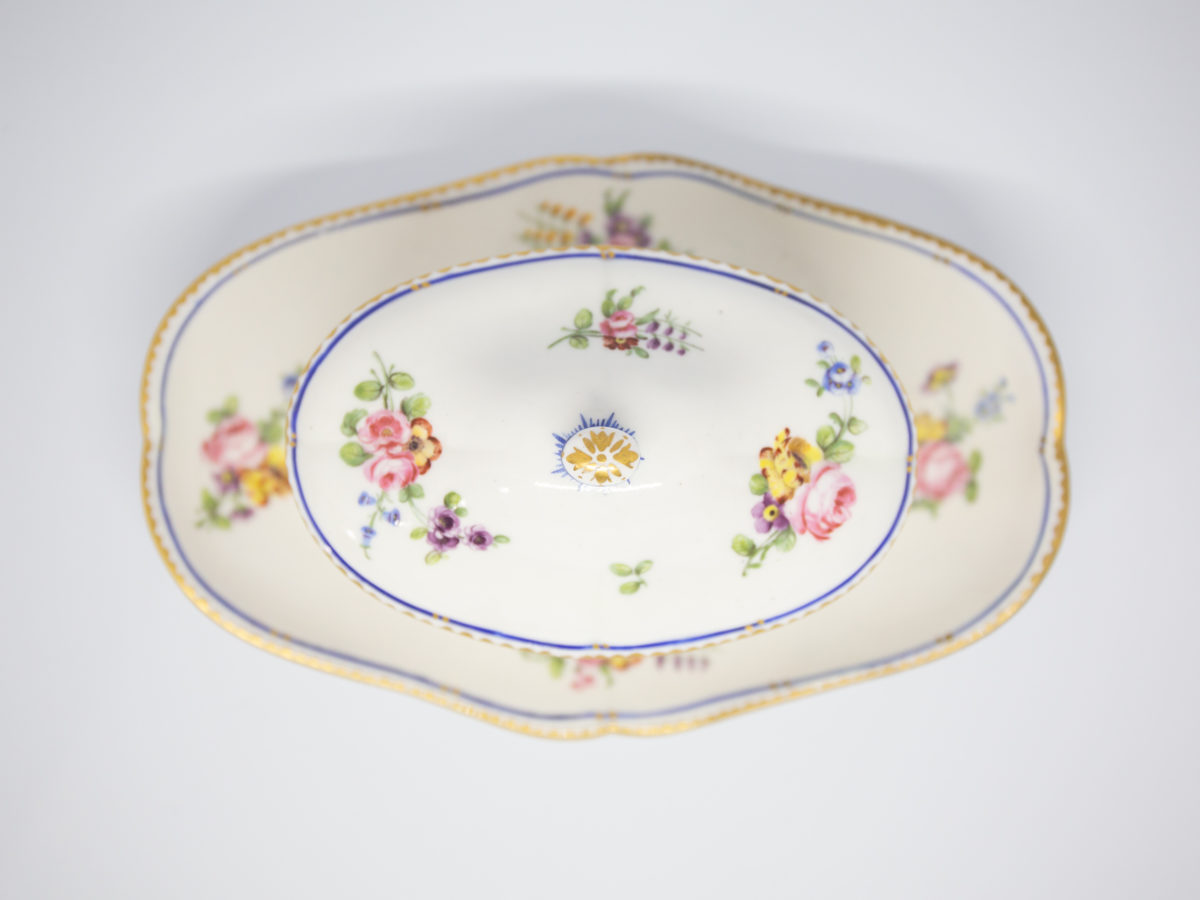 18th Century Sevres sauce boat. Soft paste porcelain sauce boat hand-painted in the feuille de choux pattern. Hairline crack to the inside of the sauce boat which does not come through under the plate. Interlaced L mark of Sevres to the base with double letter a denoting 1778. Photo of sauce boat with lid in place and shown from above looking straight down