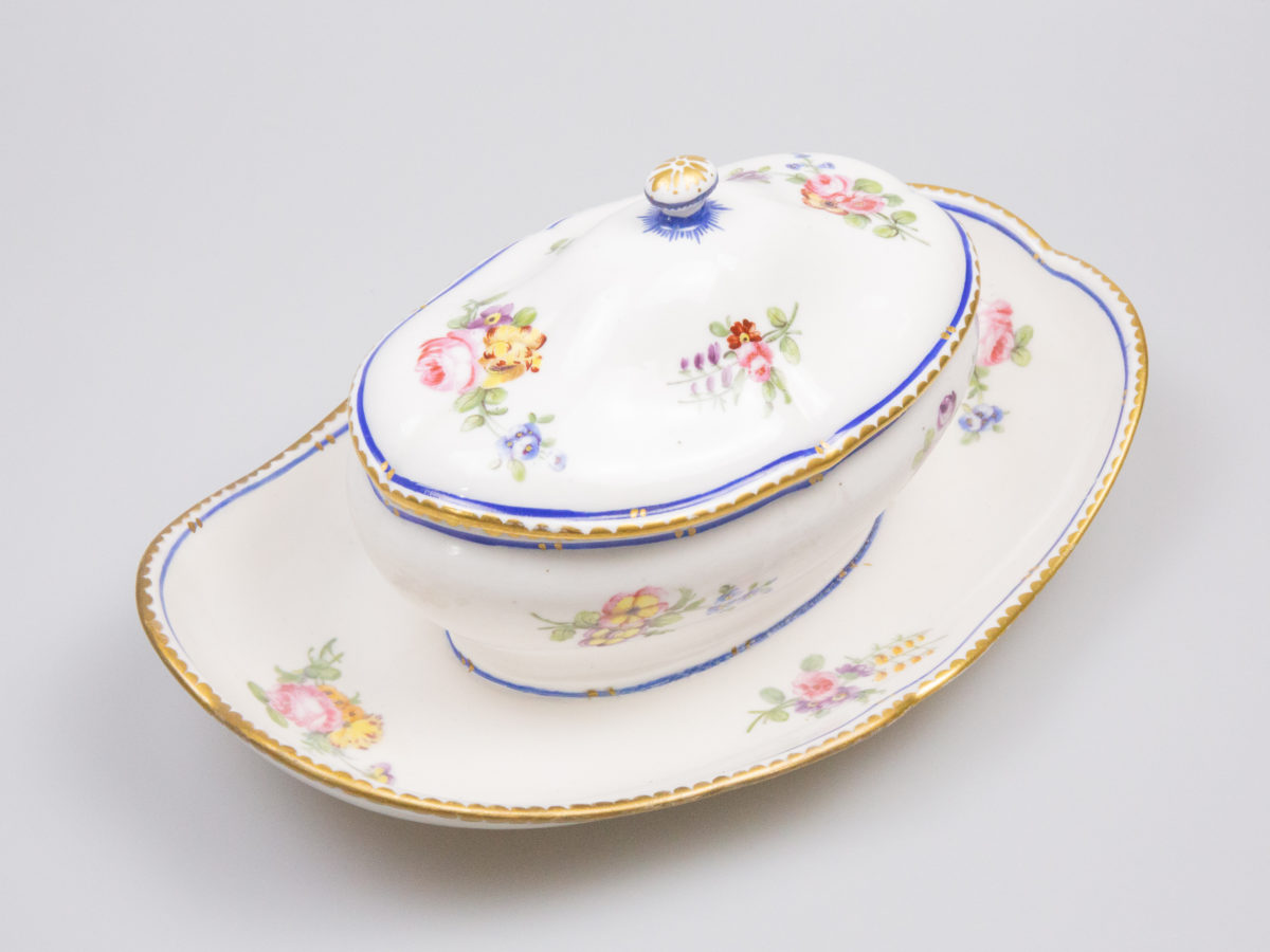 18th Century Sevres sauce boat. Soft paste porcelain sauce boat hand-painted in the feuille de choux pattern. Hairline crack to the inside of the sauce boat which does not come through under the plate. Interlaced L mark of Sevres to the base with double letter a denoting 1778. Photo of sauce boat with lid in place and seen from above. The boat is place at a diagonal angle