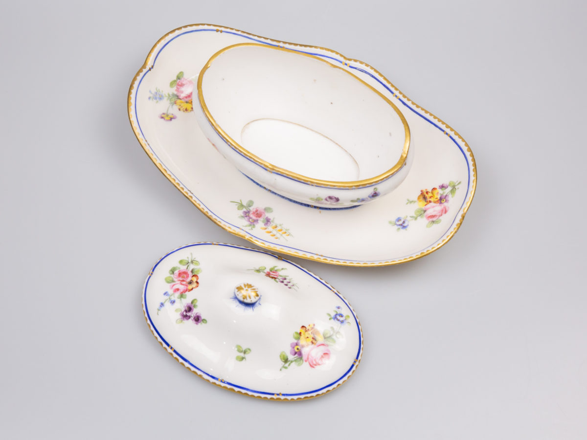 18th Century Sevres sauce boat. Soft paste porcelain sauce boat hand-painted in the feuille de choux pattern. Hairline crack to the inside of the sauce boat which does not come through under the plate. Interlaced L mark of Sevres to the base with double letter a denoting 1778. Photo of sauce boat with lid removed looking down into the boat. The lid is place alongside