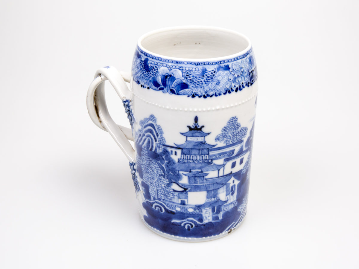 Antique Chinese blue and white tall mug. Rare mug from the Qianlong Li era c1736-1795. Decorated in classic willow pattern with an intricate and unusual 2 pleat handle. Small chip of the paint on the outer pleat handle and what appears to be a crack but most likely a consequence of the manufacturing process on the top of the inner pleat handle.  Otherwise in excellent condition for its age. Measures 82mm in diameter at base, 72mm across the top and 130mm at widest. Photo of mug showing the temple and other buildings side of mug with handle to the left of shot