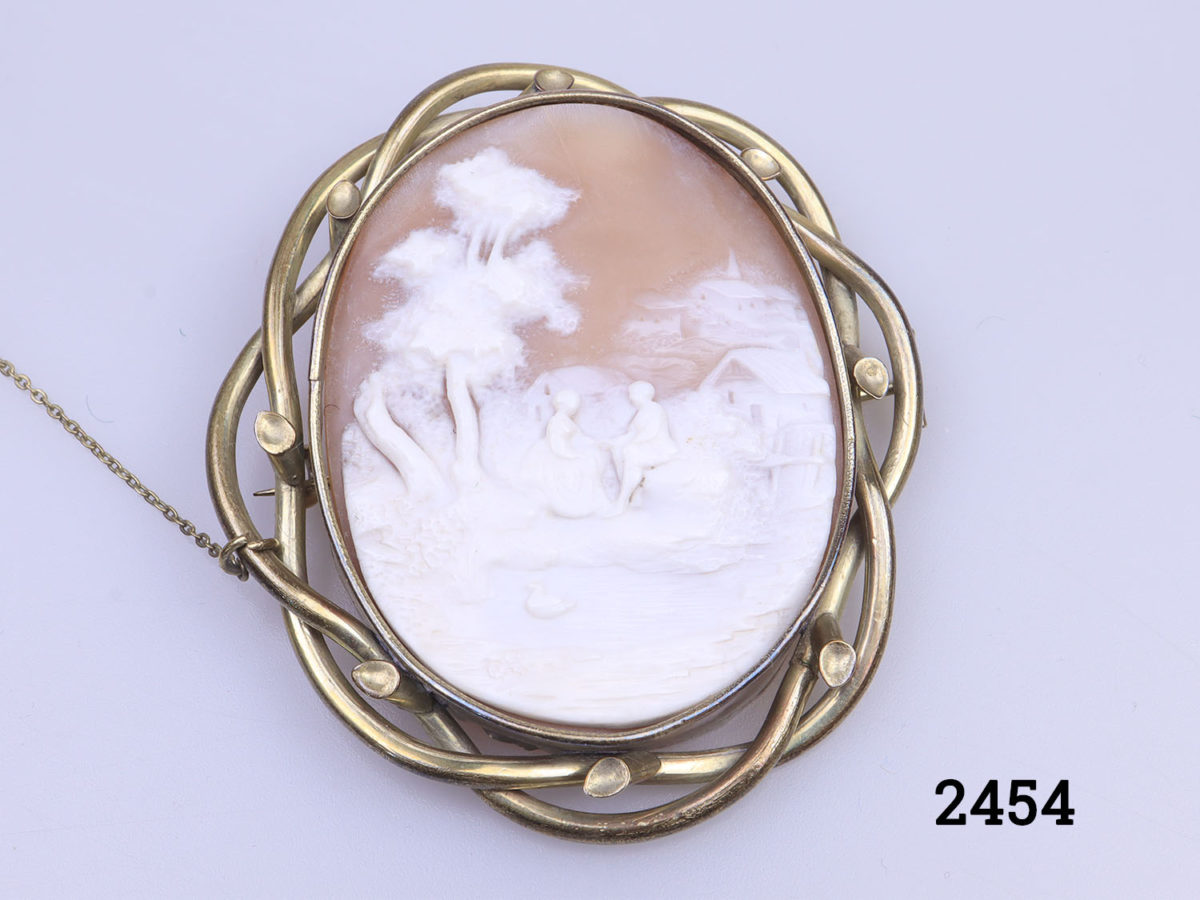 Vintage large pinchbeck cameo brooch. Intricately carved cameo of a man and woman holding hands and seated outdoors by a pond. Incredible detailing in the cameo carving. of an unusual scene. Close up photo of the cameo scene