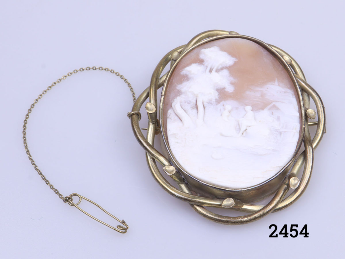 Vintage large pinchbeck cameo brooch. Intricately carved cameo of a man and woman holding hands and seated outdoors by a pond. Incredible detailing in the cameo carving. of an unusual scene. Close up photo of main photo image