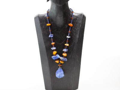 Natural amber and lapis stone necklace. Untreated natural lapis lazuli and amber bead necklace. Chunky beads put together in an indigenous style and separated with natural small lapis beads. an unusual & quite unique statement necklace. Large lapis stone at the front measures 35mm long and 32mm wide at the bottom. Main photo of necklace hanging displayed on a dark wooden stand