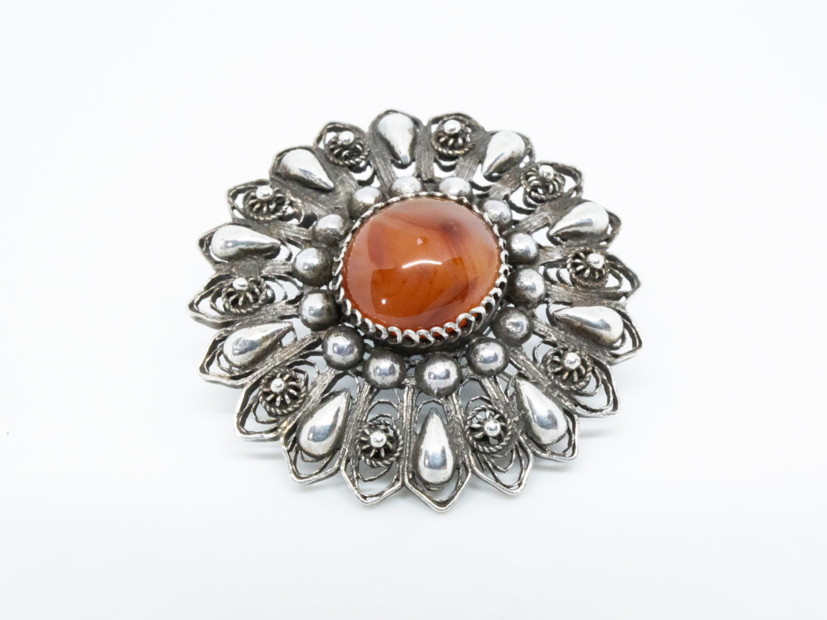 Egyptian silver brooch set with a carnelian to the centre. Intricate design of filigree work integrated with silver globules. Hallmarked to the pin. Measures 45mm in diameter. Close up photo of brooch front