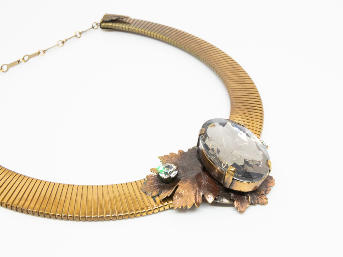 Vintage designer necklace by Ermani Bulatti. Striking design mix of Art Deco and Art Nouveau. Gilt metal choker style necklace with a bronzed leaf to the front set with a large acrylic smoky stone to the centre with Swarovski crystal to either side. Necklace is adjustable from 400mm to 485mm long. Close up photo of the front of necklace showing the decorative front design