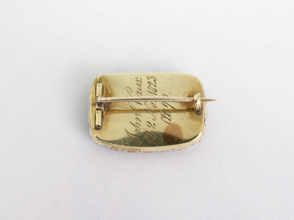 Georgian 9 karat gold mourning brooch. Small rectangular brooch with finely pleated piece of hair to the centre and framed with round cut jet stones. Beautifully inscribed in italics to the back and dated 1823. Stunning piece. Photo of back of brooch with pin closed