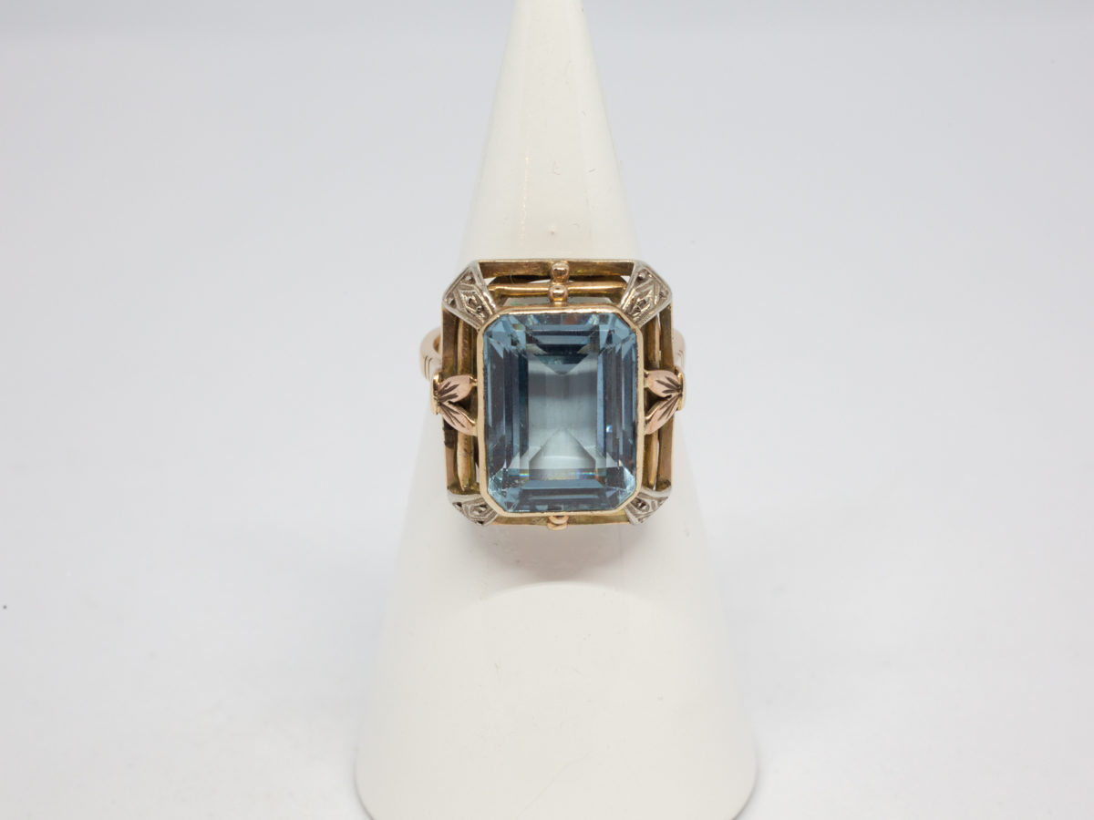 Antique 18 karat gold ring with blue topaz. c1920s large statement ring set with a large emerald cut pale blue topaz. Ring size R.5 / 8.75 Ring weight 8.6gms Main photo of ring displayed on a cone display stand with front of ring at centre facing forward.