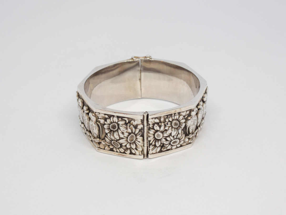 Modern chunky sterling silver bracelet. Octagonal shaped bracelet with 7 birds on a perch with flowers to either side. Hallmarked 925 for sterling silver on the clasp edge. Opens to approximately 80mm at full stretch and 60mm in diameter when closed. Photo of hinged end of bracelet with flowers.