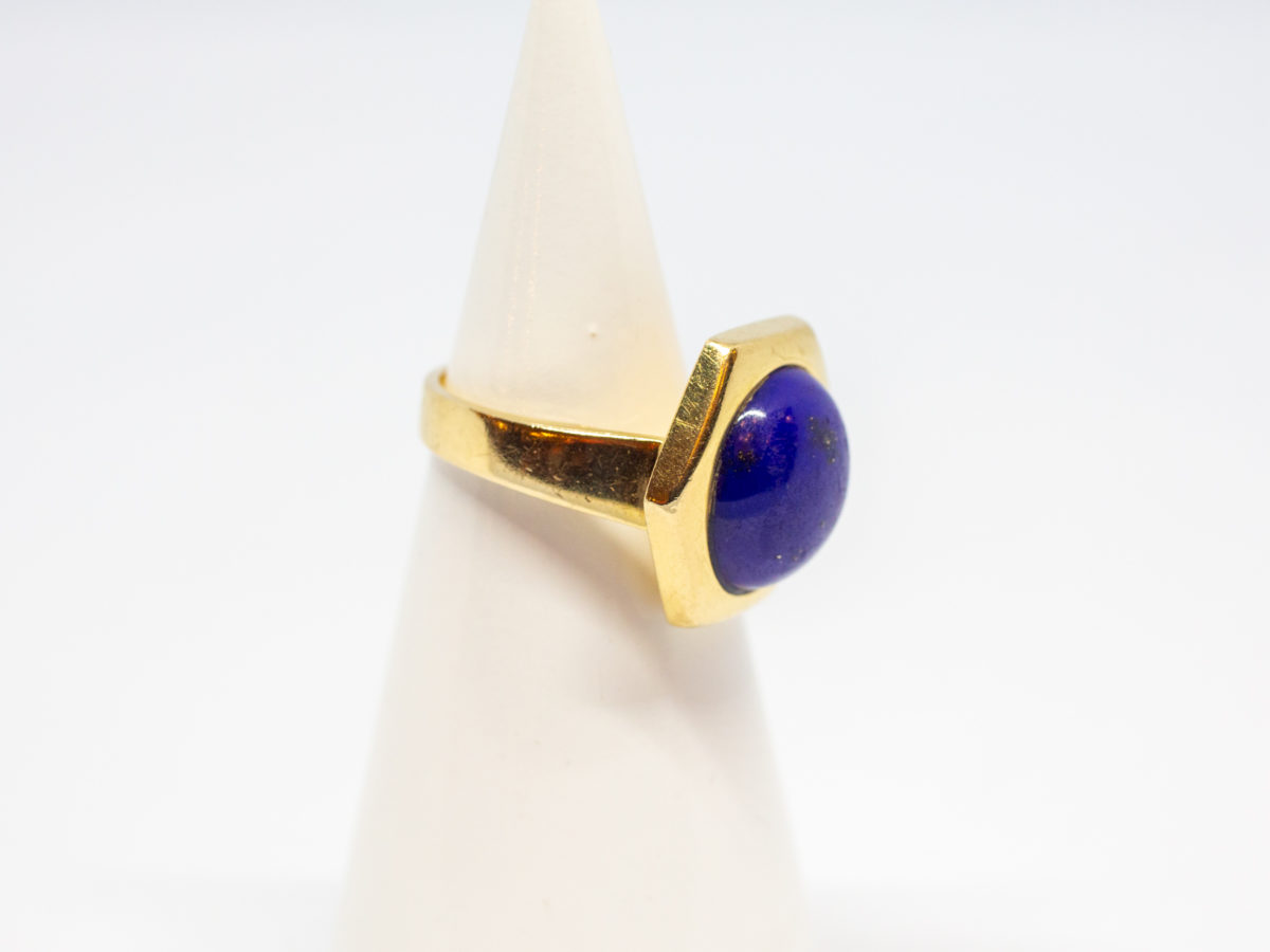 18 karat gold and lapis lazuli ring. Beautiful round lapis stone set on an unusual high hexagonal 18 karat gold mount. Size M.5 / 6.5. Weight 8.1gms. Box included. Photo of ring displayed on a cone stand with ring front facing right