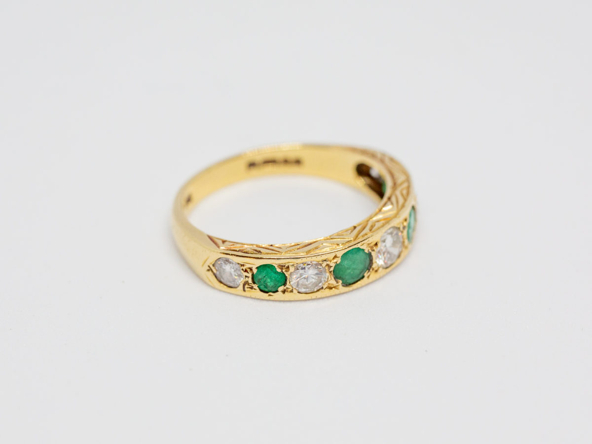 18 Karat gold, emerald and diamond. c1975 London assayed ring set with 5 round cut diamonds and 4 emeralds. Size O.5 / 7.25. Weight 3.8gms. Box included. Photo of ring on a flat surface with hallmark visible.