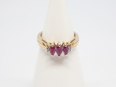 Dainty 9 karat gold and ruby. Sweet and delicate ring set with 3 marquise cut rubies with small round cut diamond to either side. Ring size M / 6.25 Weight 2.4gms. Box included. Main photo of ring displayed on a cone stand and seen from the front.