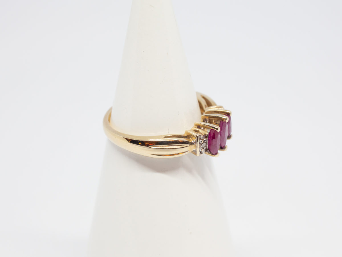 Dainty 9 karat gold and ruby. Sweet and delicate ring set with 3 marquise cut rubies with small round cut diamond to either side. Ring size M / 6.25 Weight 2.4gms. Box included. Photo of ring displayed on a cone stand and seen with stones facing right.