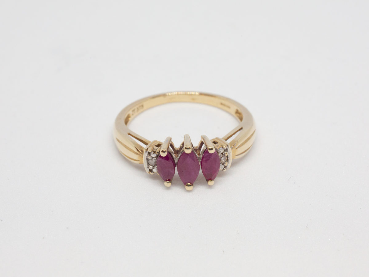 Dainty 9 karat gold and ruby. Sweet and delicate ring set with 3 marquise cut rubies with small round cut diamond to either side. Ring size M / 6.25 Weight 2.4gms. Box included. Photo of ring on a flat surface and seen from the front