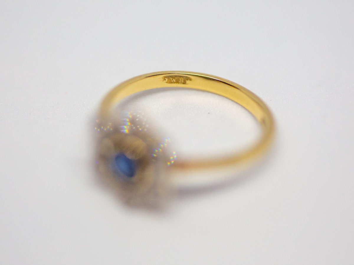Art Deco sapphire and diamond ring. Pretty ring in the form of a flower with a stunning blue round cut sapphire to the centre with 6 small round cut diamonds on each outer petal. Set on 18 karat yellow gold. Ring size L / 5.75. Weight 2.8gms. Box included. Close up photo of the makers initials on the inside band