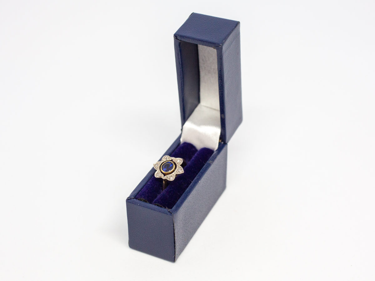 Art Deco sapphire and diamond ring. Pretty ring in the form of a flower with a stunning blue round cut sapphire to the centre with 6 small round cut diamonds on each outer petal. Set on 18 karat yellow gold. Ring size L / 5.75. Weight 2.8gms. Box included. Photo of ring displayed in box (included)