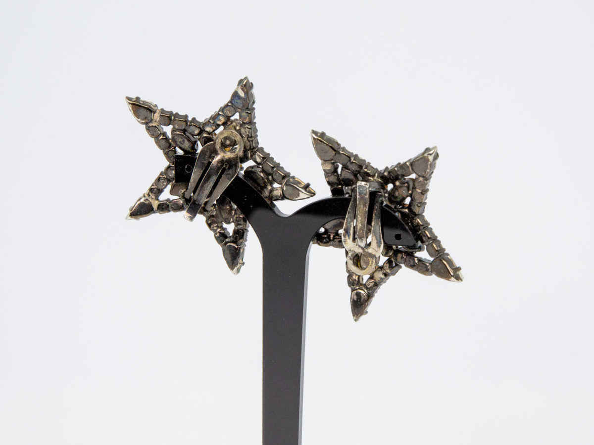 Vintage 1980s Butler & Wilson earrings. Large rhinestone starburst clip-on earrings. Marked B&W to the back. Both clips are in good working order. Each earring measures approximately 50mm in diameter. Photo of earrings on a display stand and seen from the back
