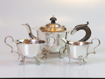 Edwardian sterling silver bachelor tea service. Wonderful tea service set comprising of a small tea pot, sugar bowl and milk jug. Each piece has a fluted edge with the tea pot and sugar bowl on 4 feet and jug on 3 feet. Hallmarked for Birmingham assay and dated 1909 to each piece. Made by Joseph Gloster Ltd. Some minor signs of wear. The tea pot has a Bakelite finial and handle and measures approximately 220mm from tip of spout to edge of handle, 135mm wide across the top, 135mm tall to tip of finial and 70mm square at the 4 feet. Sugar bowl measures 155mm edge to edge at handles, 110mm across the top, 80mm tall from feet to highest point at handle tips, 65mm tall from feet to edge of bowl and 60mm square at the 4 feet. Jug measures 118mm from tip of spout to handle edge, 88mm across the top, 80mm tall from feet to top of handle. 75mm from feet to tip of spout, 60mm from feet to jug edge and 60mm across the 3 feet. Main photo of all 3 pieces displayed together with tea pot in background, sugar bowl to left and jug to right