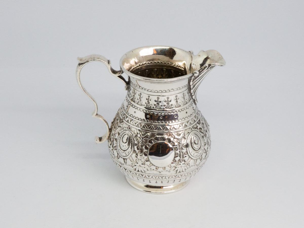 c1875 Small sterling silver jug. Very sweet and finely decorated small jug by Barnard & Sons Ltd. Full hallmark to the base for London assay. Stunning piece with empty cartouche to either side for personalisation. Measures 40mm in diameter at the base, 85mm from tip of spout to edge of handle and 45mm across the top. Photo of jug seen from the side and slightly raised with spout to the right of photo