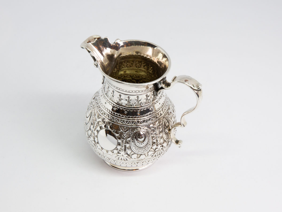 c1875 Small sterling silver jug. Very sweet and finely decorated small jug by Barnard & Sons Ltd. Full hallmark to the base for London assay. Stunning piece with empty cartouche to either side for personalisation. Measures 40mm in diameter at the base, 85mm from tip of spout to edge of handle and 45mm across the top.  Photo of jug from a slight raised angle showing partial interior of jug (handle to the bottom right of photo)