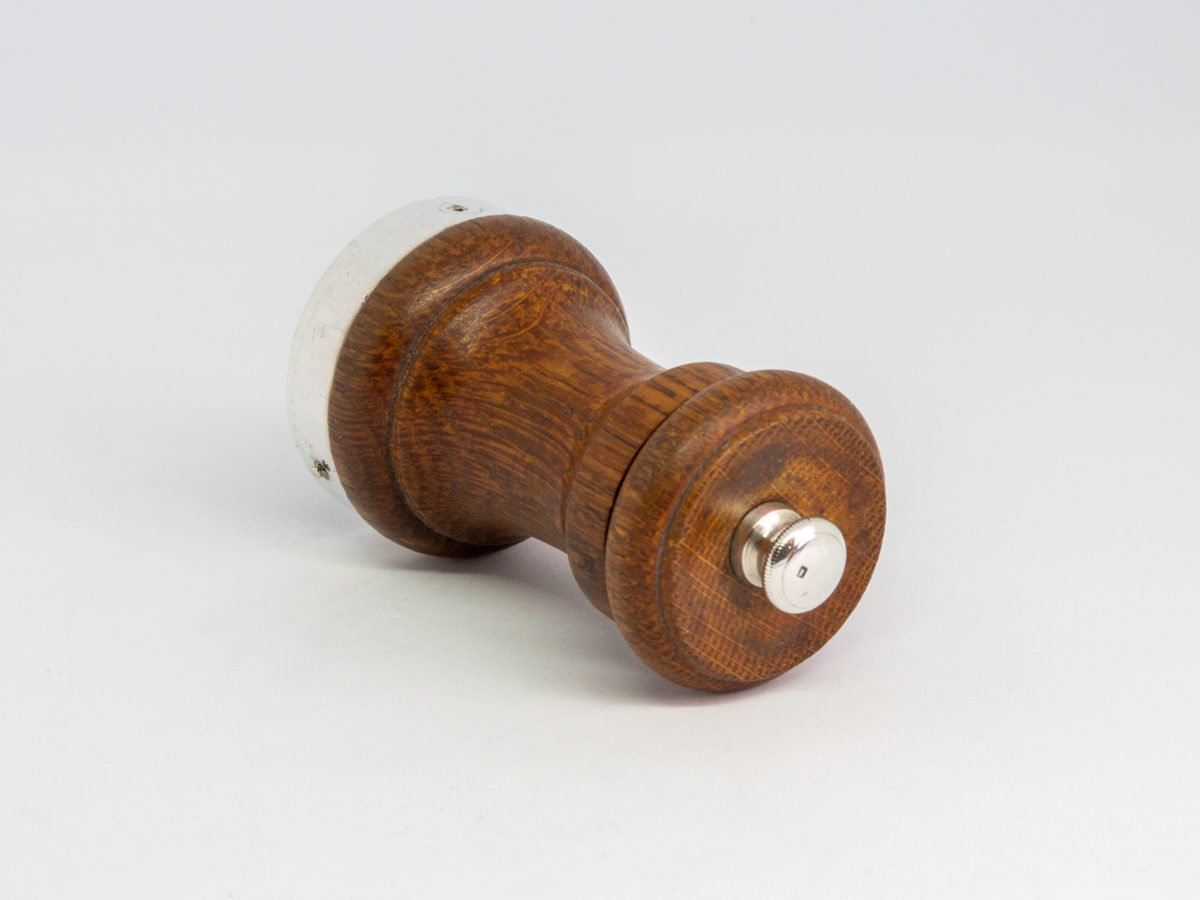 c1932 Small pepper grinder. Petite pepper grinder with oak body and silver top and base rim. The best in pepper grinders with a Peugeot movement. Hallmarked to the base for Birmingham assay and made by John Grinsell & Sons. Lion passant to the top. Measures 45mm in diameter at base and 42mm in diameter at top. Photo of grinder shown laid on side with top end in the foreground
