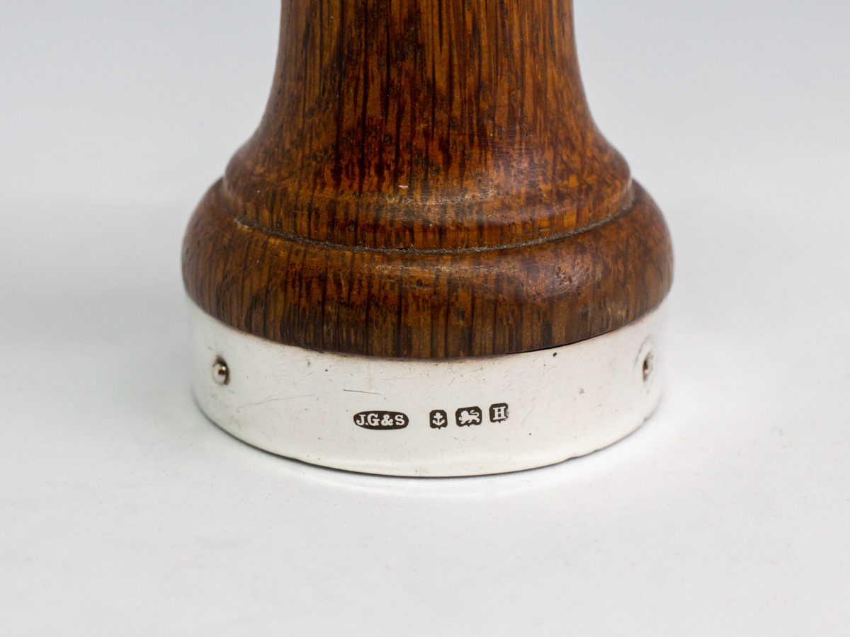 c1932 Small pepper grinder. Petite pepper grinder with oak body and silver top and base rim. The best in pepper grinders with a Peugeot movement. Hallmarked to the base for Birmingham assay and made by John Grinsell & Sons. Lion passant to the top. Measures 45mm in diameter at base and 42mm in diameter at top. Close up photo of the hallmark on the base rim of grinder