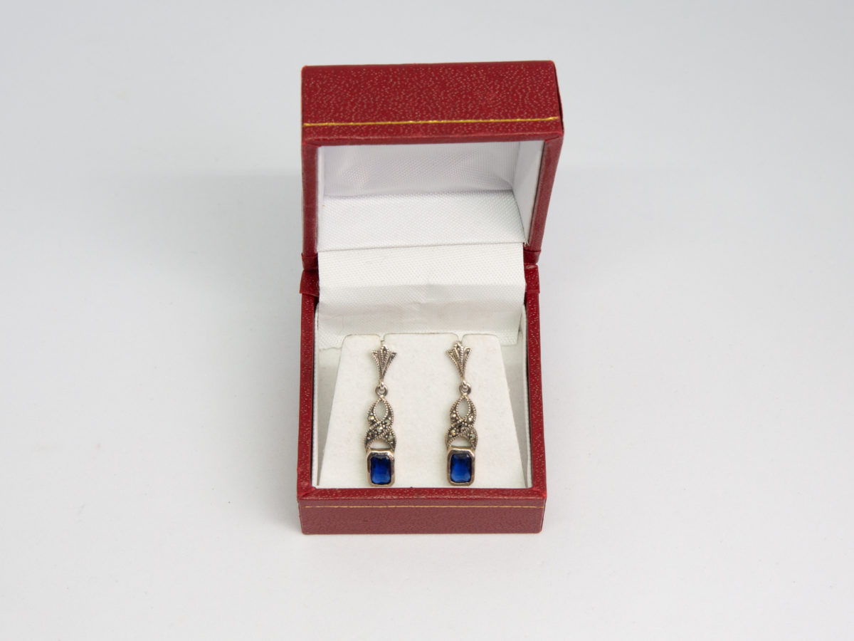Art Deco style sterling silver earrings. Vintage earrings in a Deco style with marcasite and blue glass detail. Hallmarked 925 for sterling silver to back of earrings and butterfly fasteners. Box included. Earring drop length approximately 30mm. Earrings weight 2.8gms. Photos of earrings displayed in a red box