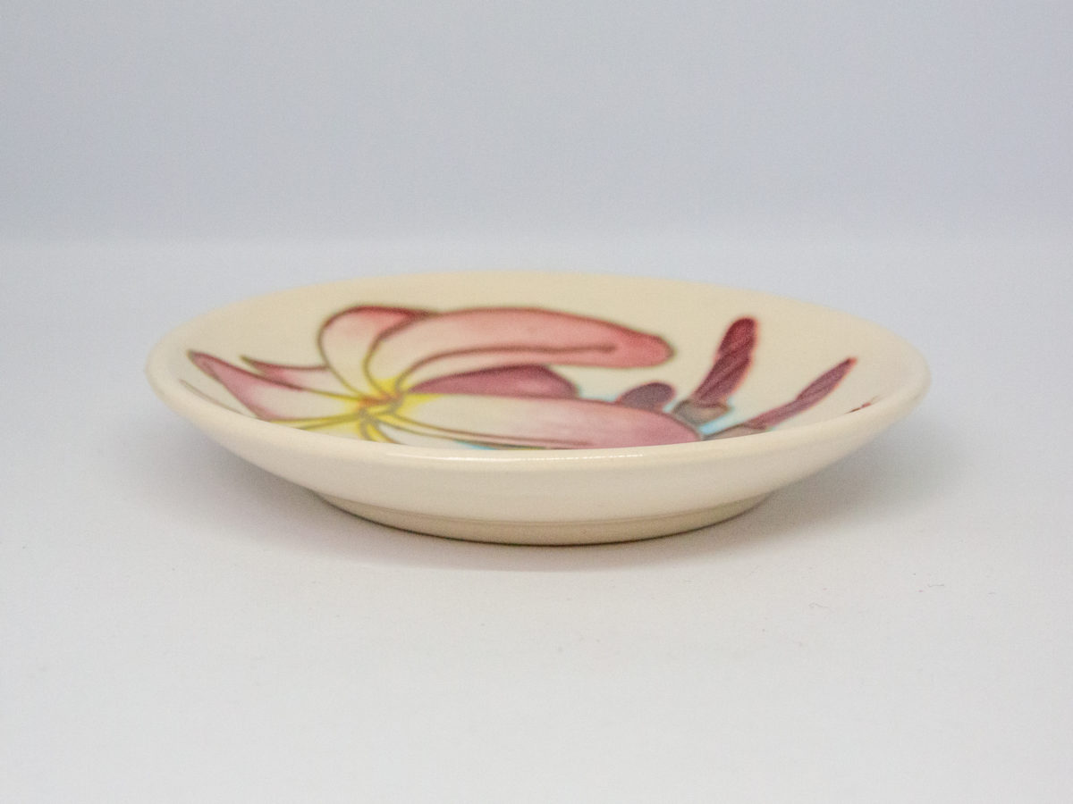 Moorcroft Frangipani Plumeria dish. Small round dish in cream with frangipani plumeria blossom. Stamped Moorcroft to the back and dated c1999. Measures 120mm in diameter and 75mm at base. Photo of dish from a near eye level angle showing the depth