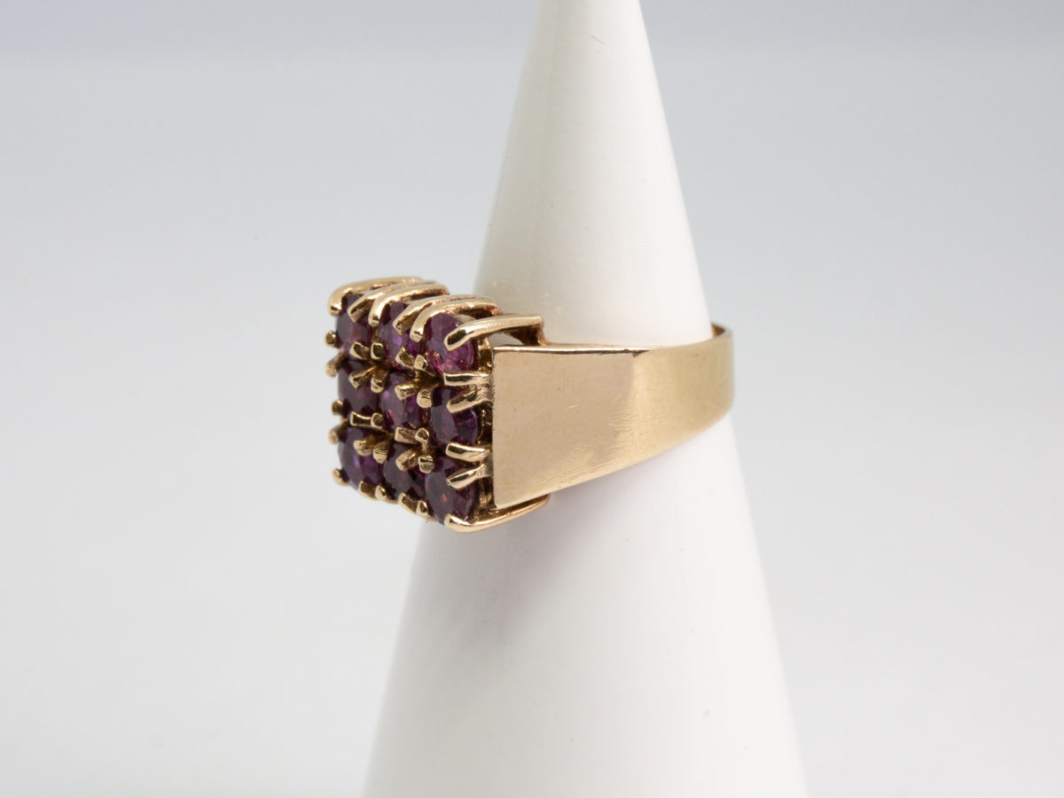 c1976 9 karat gold and ruby ring. Vintage ring in solid 9 karat gold with 9 round cut pink rubies set on a square setting. Ring size N / 6.75 Ring weight 5.4gms. Photo of ring displayed on a cone with ring front facing left of picture.