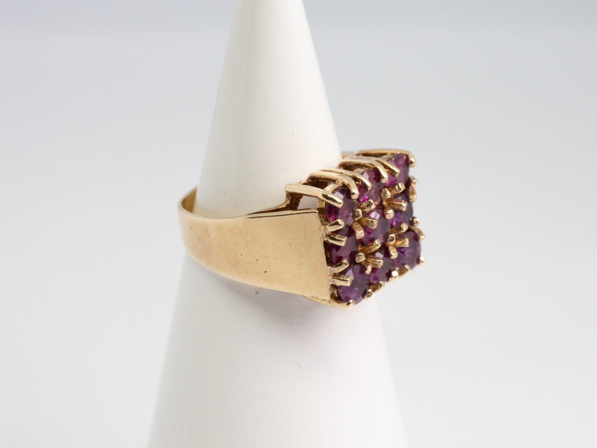 c1976 9 karat gold and ruby ring. Vintage ring in solid 9 karat gold with 9 round cut pink rubies set on a square setting. Ring size N / 6.75 Ring weight 5.4gms. Photo of ring on a display cone with ring front facing right of photo.