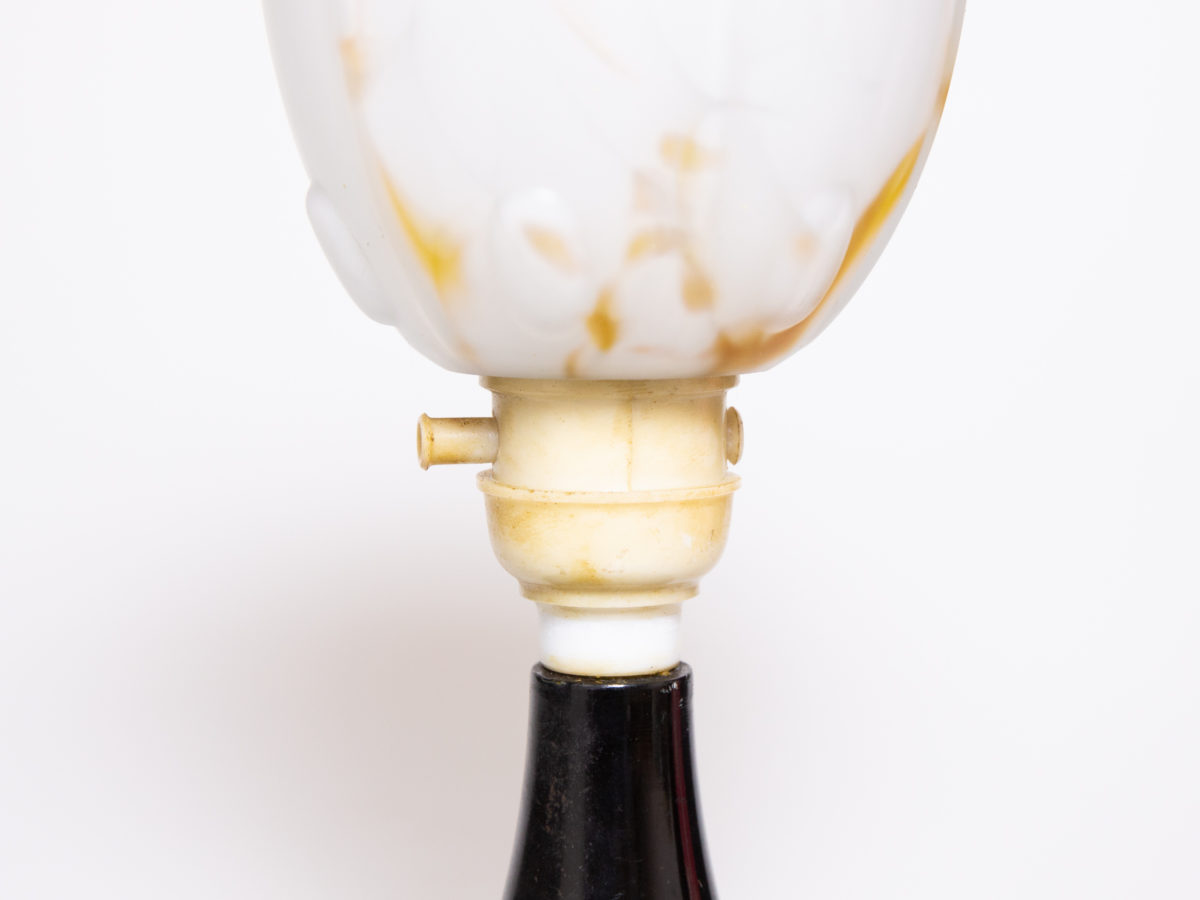 1930s Art Deco lamp with Bakelite base. Small up-lighting lamp with marble effect glass shade in cream with caramel coloured flecks on a moulded brown/black Bakelite base. Base measures 128mm in diameter and top of lamp measures 132mm in diameter. Close up photo of the switch area of lamp between the dark Bakelite base and lampshade.