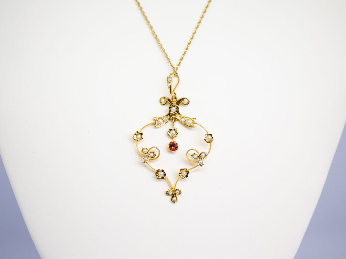 Edwardian 15 karat gold Lavaliere pendant on 9 karat gold chain. Very pretty Edwardian pendant set with seed pearls and a single hanging garnet to the centre. Hallmarked 15ct to the back. Chain is 9 karat gold and fully hallmarked on the clasp and clasp ring for Birmingham assay. Pendant drop length 55mm and 32mm at widest. Chain measures 460mm long. Whole necklace weighs 5.6gms. Close up photo of the lavaliere pendant shown on a display stand.