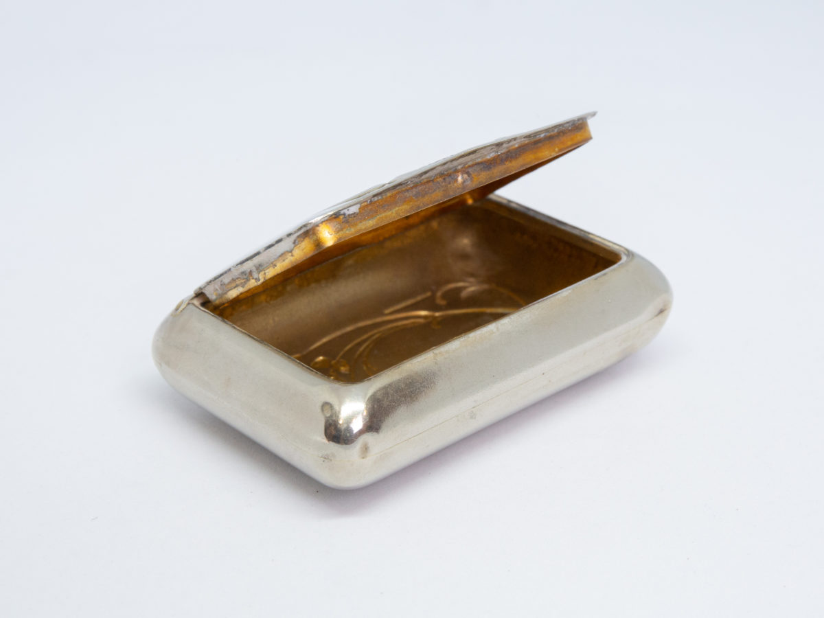 Art Nouveau Continental snuff box. Pretty silver plated snuff box with gilt interior. Decorated with an image of a pilgrim at the shrine of Our Lady of Lourdes to the lid and very typical Art Nouveau floral decoration on the base. In very good condition throughout with only a few dinks at the corners. Photo of box with lid open and shown at a diagonal and near eye level angle with gilt wear to the inner rim of lid visible.
